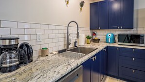 A modern kitchen with dark blue cabinets, a stainless steel sink, a coffee maker, a microwave, and a kettle.