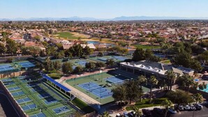 Vue aérienne d’un quartier résidentiel comprenant plusieurs courts de tennis, un terrain de golf et un grand bâtiment doté d’un toit plat.