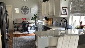 Une cuisine moderne avec des meubles blancs, un plan de travail en marbre et un coin repas comprenant une table et des chaises en bois.
