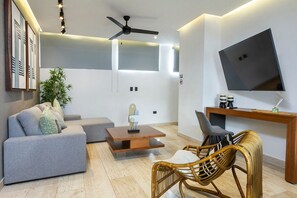 A modern living room with a sofa, a coffee table, a chair, a TV mounted on the wall, and a ceiling fan. - Modern apartment near Fifth Avenue (Playa del Carmen)