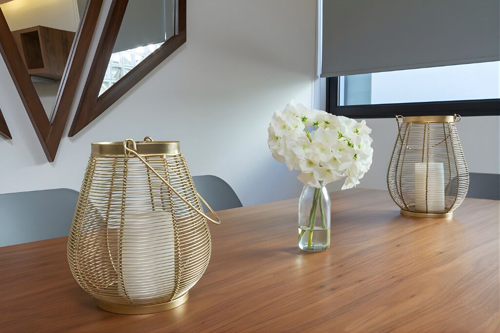 Een houten tafel met twee gouden draadlampen en een vaas witte bloemen.