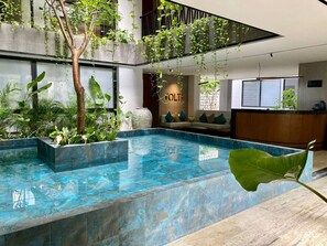 An indoor swimming pool with a modern design, surrounded by various plants and a seating area with a reception desk. - Modern Apartment Near Fifth Avenue (Playa del Carmen)