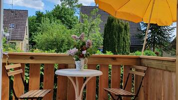 Eine Holzterrasse mit Tisch und zwei Stühlen, einem gelben Sonnenschirm und einem Blumenstrauß.