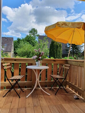 A wooden deck with a table and two chairs, a yellow umbrella, and a vase of flowers. - Sea period vacation apartment (Neustadt in Holstein)