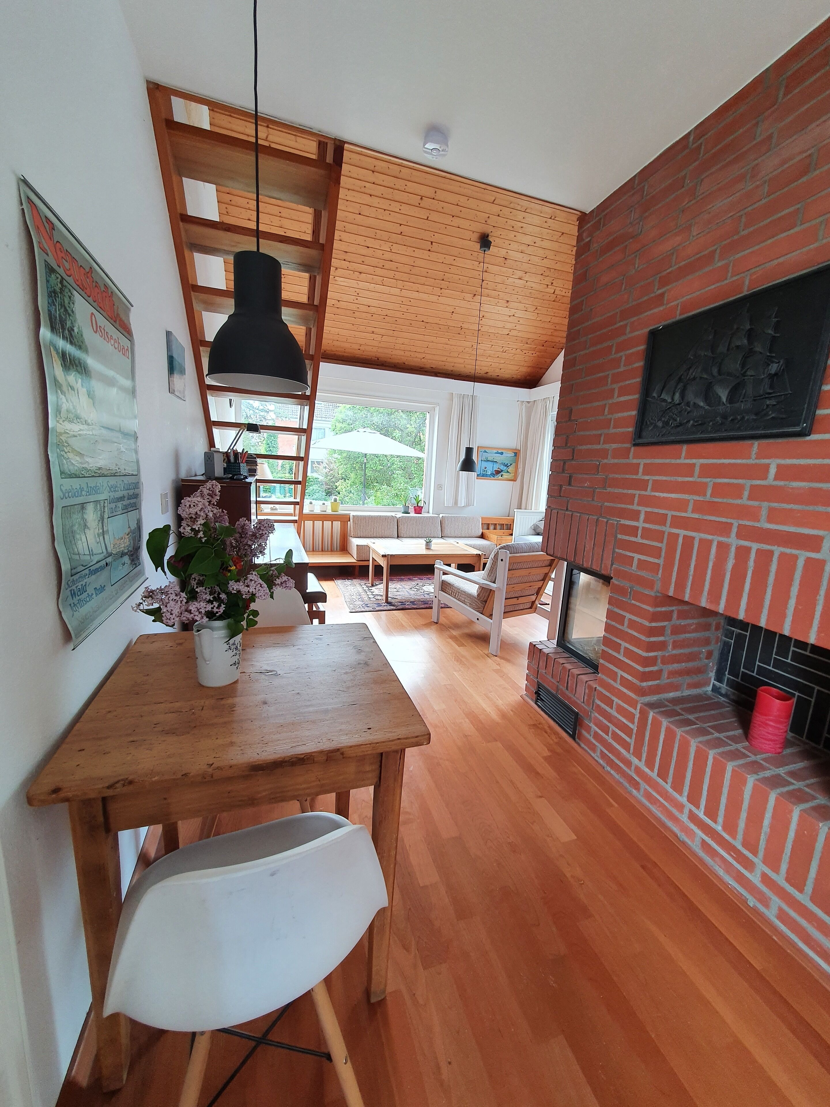 Ein gemütliches Zimmer mit einem Holzespeisetisch, einem weißen Stuhl, einem Backsteinofen und einem großen Fenster.