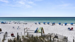 Una playa con arena blanca, sombrillas azules y sillas de playa.