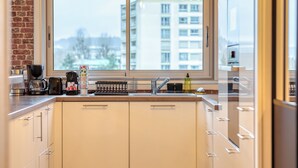 Moderni keittiö, jossa on suuri ikkuna, kahvinkeitin, vedenkeitin ja astiateline.
