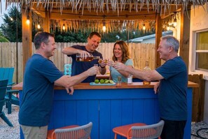 A wooden bar with a thatched roof, surrounded by outdoor seating. - Backyard Oasis • Pool •  Hot Tub • Putt Putt • Bar (Largo)