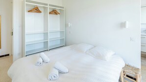 A bedroom with a large bed, a wardrobe with hanging space, and a bedside table. - Spectacular 2-Bedroom Apartment with Sea View – Market Square (LE LAVANDOU)
