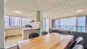 A modern living room with a wooden dining table, grey sofas, and a view of the ocean. - Luxury 2 Bedroom Ocean View Apartment in Surfers Paradise (Surfers Paradise)