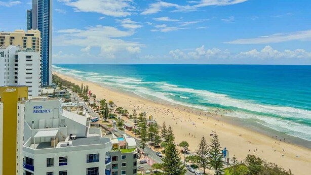 A coastal cityscape with a beach, high-rise buildings, and a Surf Regency hotel. - Luxury 2 Bedroom Ocean View Apartment in Surfers Paradise (Surfers Paradise)