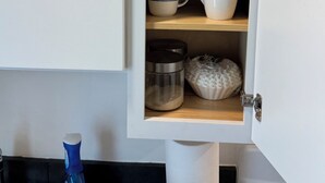 Een keukenkastje met een pak koffieroom, een koffiezetapparaat en een zak koffiecups.