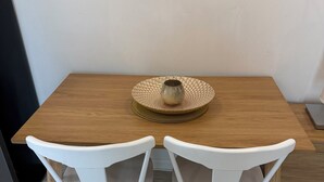 Een eettafel met twee witte stoelen, een geweven placemat en een kleine keramieken pot op tafel.