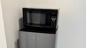 Een koelkast van roestvrij staal met een ingebouwde magnetron erboven, geplaatst tegen een witte muur.