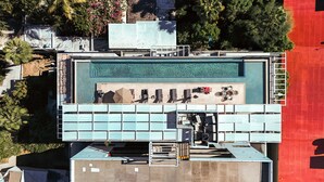 Et luftfoto viser et hotel med swimmingpool på taget, flere balkoner og en rød sti.