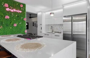 Une cuisine moderne dotée d’un îlot central, d’appareils électroménagers en acier inoxydable et d’un mur végétal agrémenté de fleurs.