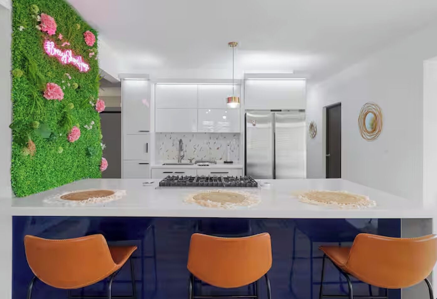 Eine moderne Küche mit weißen Schränken, einer zentralen Kochinsel mit Barhocker und einer grünen Wand mit rosa Blumen.