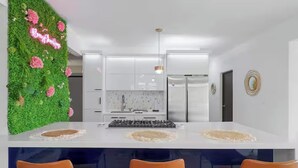 Eine moderne Küche mit weißen Schränken, einer zentralen Kochinsel mit Barhocker und einer grünen Wand mit rosa Blumen.