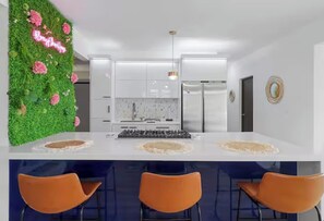 A modern kitchen with white cabinets, a central island with stools, and a green wall with pink flowers. - Family Beach Escape • Private Pool • Ocean View • Sleeps 8 (De Hatillo)