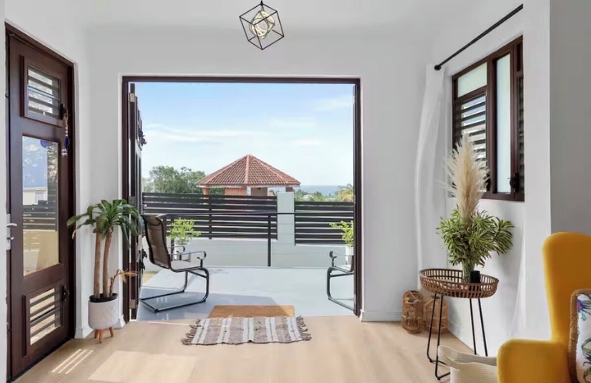 A modern interior with a sliding glass door leading to a balcony, a yellow chair, and potted plants.