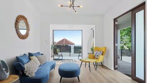 Ein modernes Wohnzimmer mit einem blauen Sofa, einem gelben Sessel und einem großen Fenster mit Blick auf ein Gebäude mit rotem Dach.