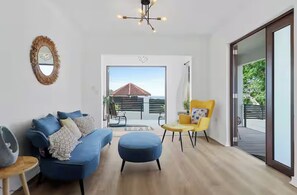 A modern living room with a blue sofa, a yellow armchair, and a large window offering a view of a red-roofed building. - Family Beach Escape • Private Pool • Ocean View • Sleeps 8 (De Hatillo)