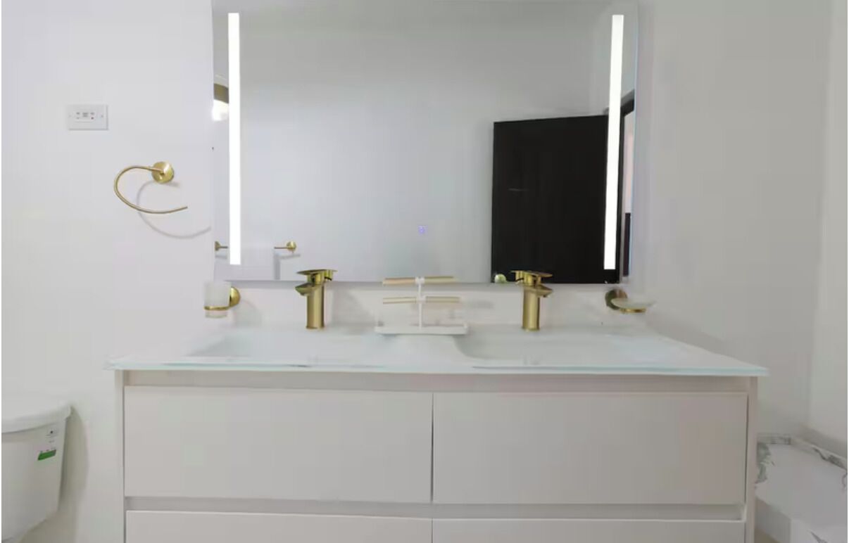A bathroom with a white vanity, a large mirror, and gold fixtures.