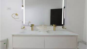 A bathroom with a white vanity, a large mirror, and gold fixtures.
