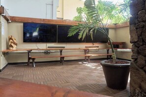 A room with a large potted plant, wooden benches, and a flat-screen TV mounted on the wall. - Charm near Waikiki Beach! (Honolulu)