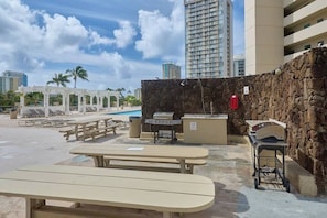 Un espace extérieur aménagé en terrasse, avec des tables de pique-nique, un barbecue et un mur en pierre.