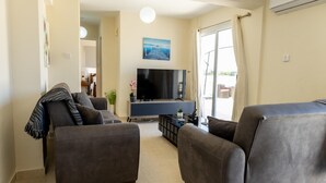 A living room with a flat-screen TV, two sofas, a coffee table, and a sliding glass door leading to an outdoor area. - Penthouse Apartment Sleeps 4 - Sea Views, Pool (Kapparis)