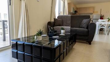 A modern living room with a black modular coffee table, a sofa, and a kitchen area in the background.