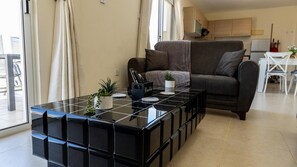 A modern living room with a black modular coffee table, a sofa, and a kitchen area in the background. - Penthouse Apartment Sleeps 4 - Sea Views, Pool (Kapparis)