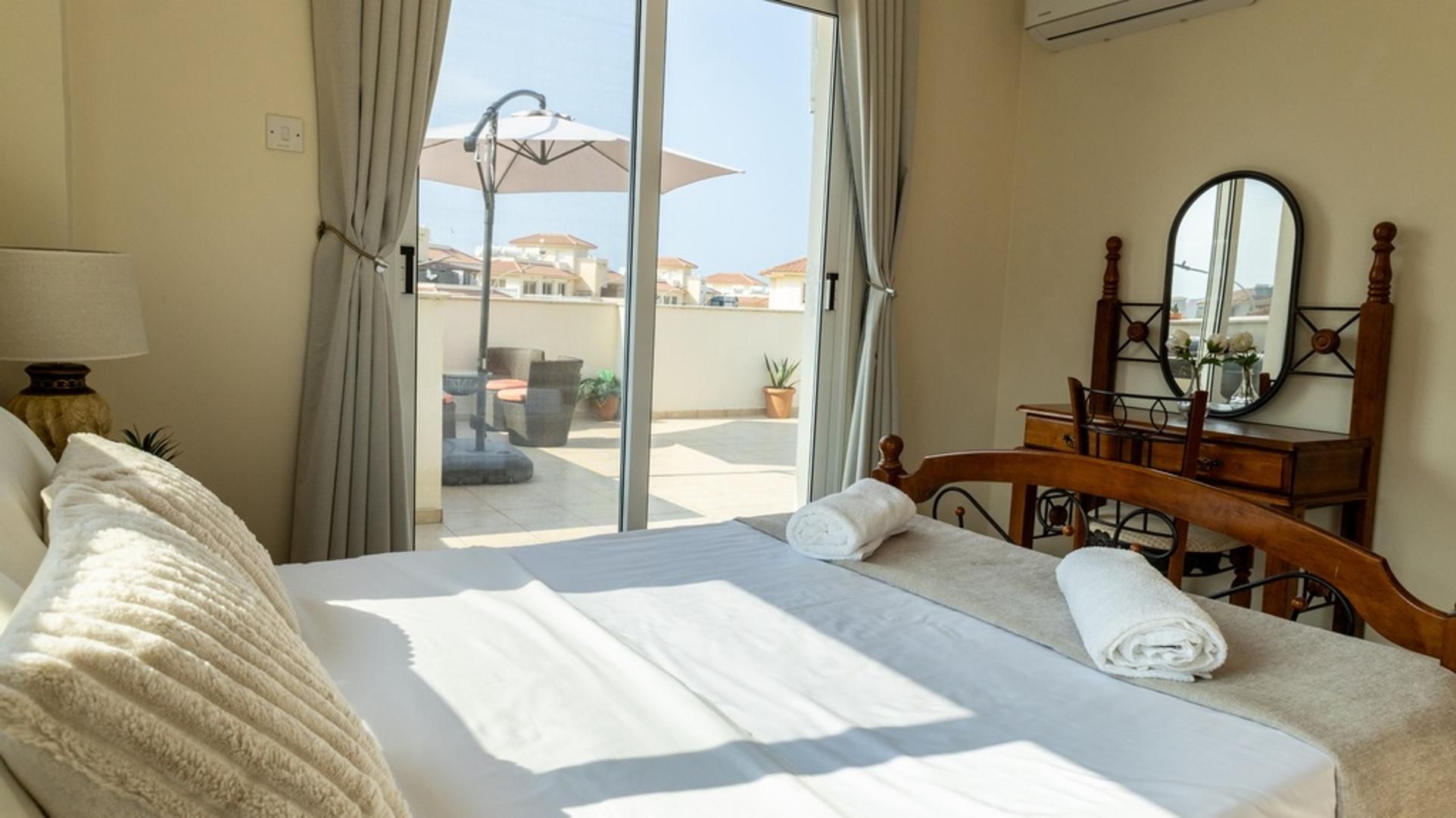 A hotel room with a bed, a wooden dresser, a mirror, and a view of the outdoor area.