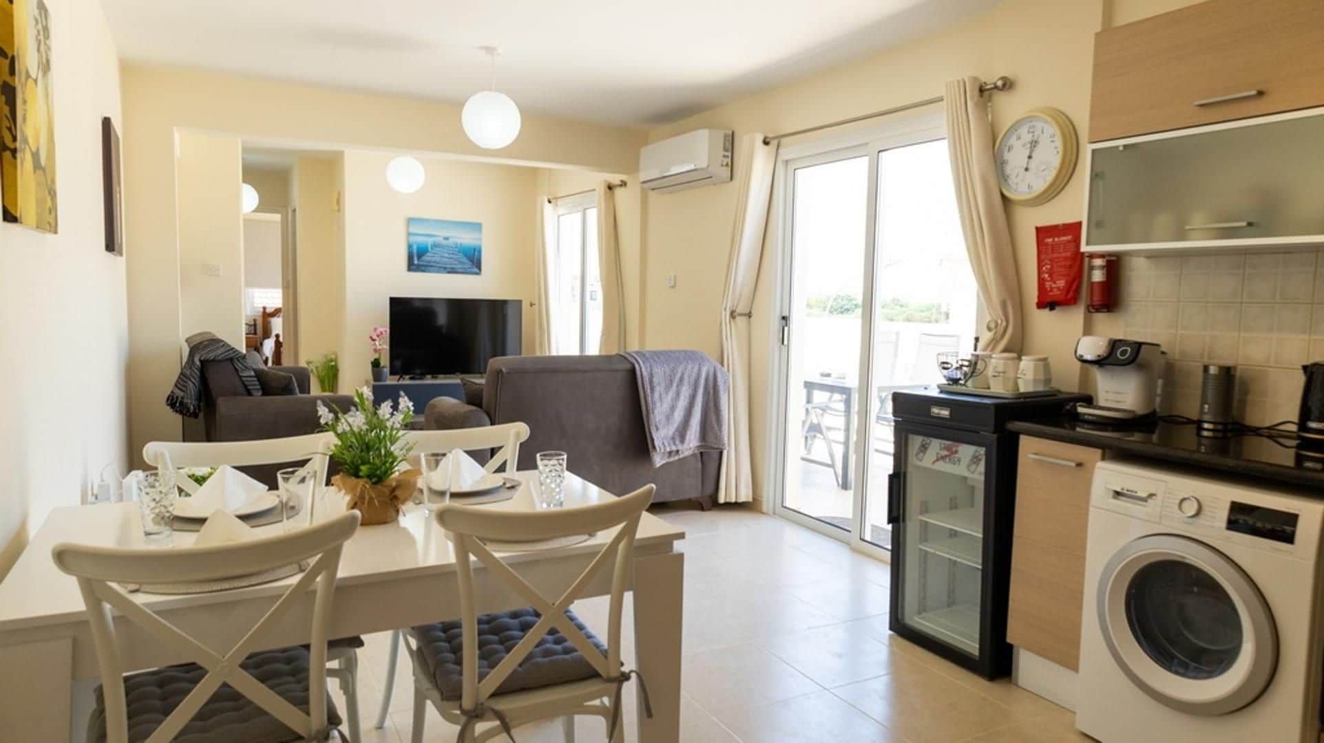 Un espace de vie compact comprenant un coin repas, un canapé, un téléviseur, une cuisine équipée et un lave-linge.