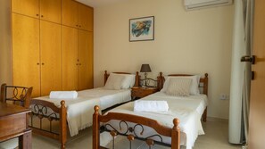 A bedroom with two single beds, a wooden wardrobe, a desk, and a wall-mounted air conditioner. - Penthouse Apartment Sleeps 4 - Sea Views, Pool (Kapparis)