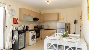 A compact kitchen with a washing machine, microwave, and refrigerator. - Penthouse Apartment Sleeps 4 - Sea Views, Pool (Kapparis)