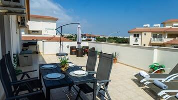 A rooftop terrace with a table set for two, outdoor furniture, and a view of the surrounding buildings.