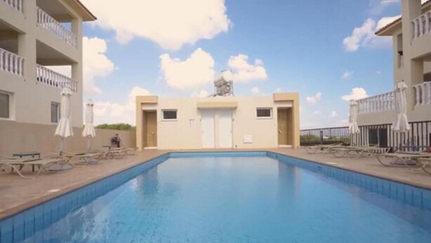 A swimming pool with a clear blue water surface, surrounded by a low fence. There are lounge chairs and umbrellas on the poolside. - Penthouse Apartment Sleeps 4 - Sea Views, Pool (Kapparis)