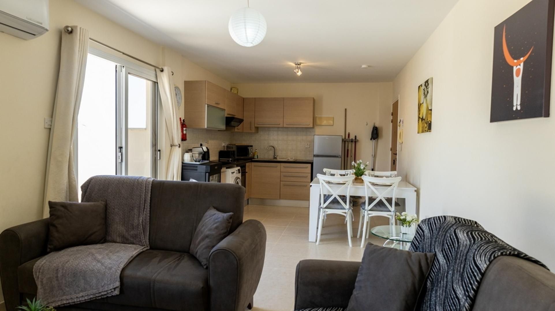 A compact living space with a sofa, a dining table with chairs, a kitchen area, and a small balcony.