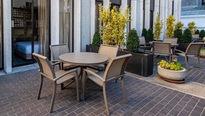 An outdoor seating area with a round table and chairs, surrounded by potted plants and a brick floor.
