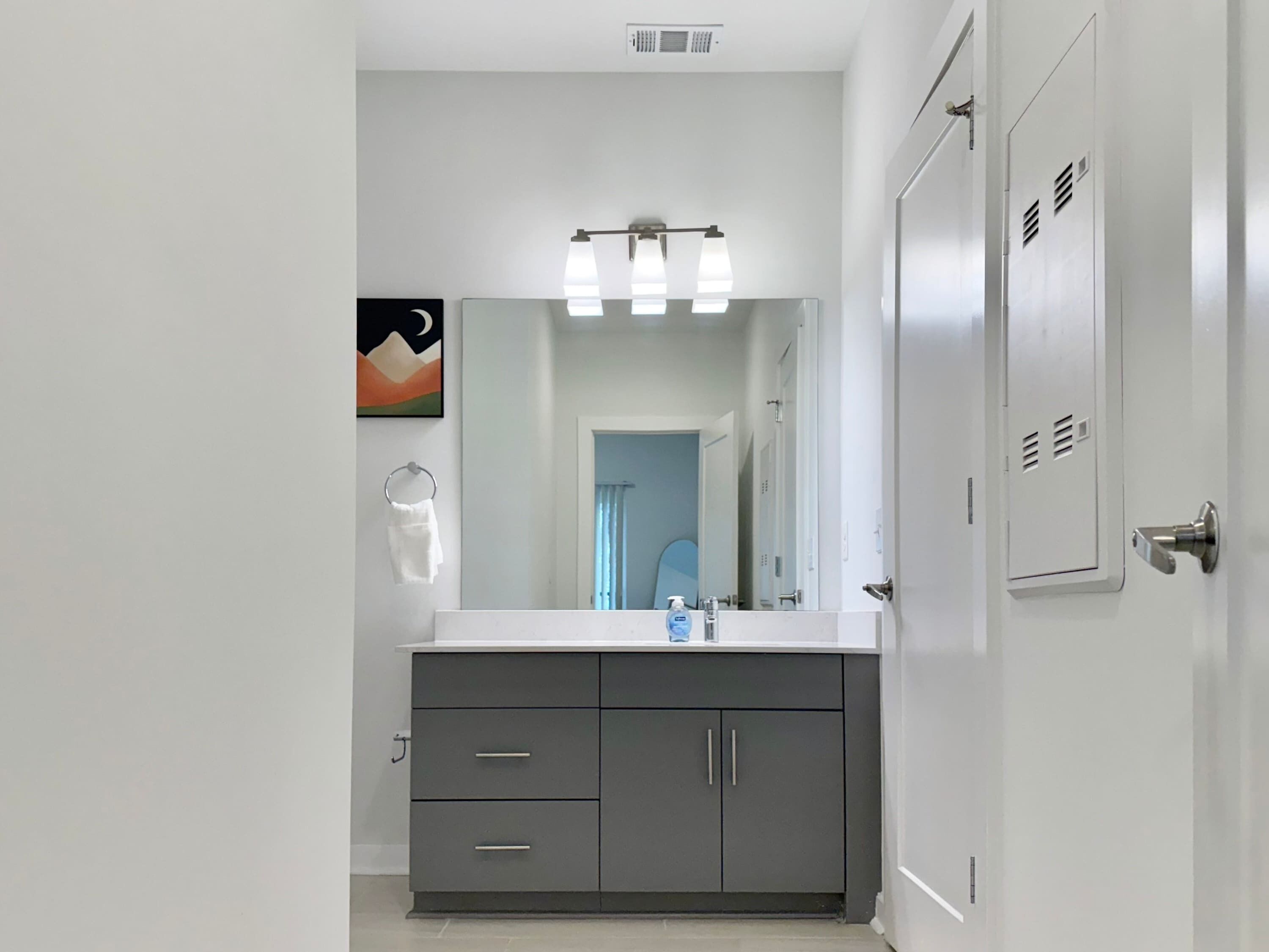 A modern bathroom with a large mirror, a white sink, and grey cabinets.