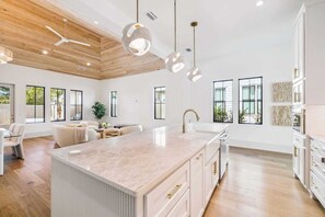 A spacious kitchen with a large island, modern pendant lights, and a high ceiling with wooden beams. - Pristine 4BR Beach Getaway! Golf Cart included! 4 Bikes! Private Pool! Close to Beach! ~ Sweet Bay (Panama City Beach)