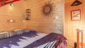 A wooden cabin room with a bed, a mirror, a framed picture, and skis hanging on the wall. - ô LIMPâR - HAUTELUCE - Gîte (HAUTELUCE LES SAISIES)