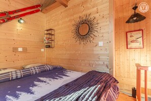 Ein Zimmer in einer Holzhütte mit einem Bett, einem Spiegel, einem gerahmten Bild und aufhängten Skiern an der Wand.
