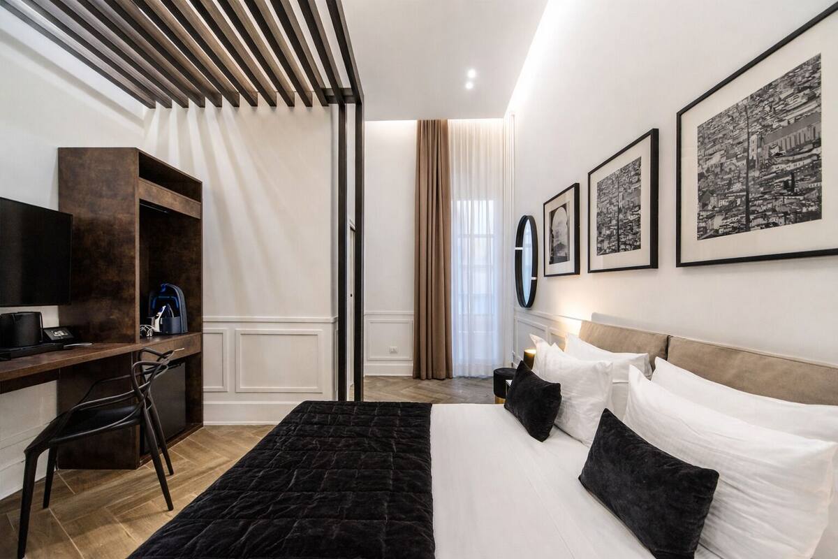 A modern hotel room with a large bed, a desk with a laptop, a chair, and a TV.