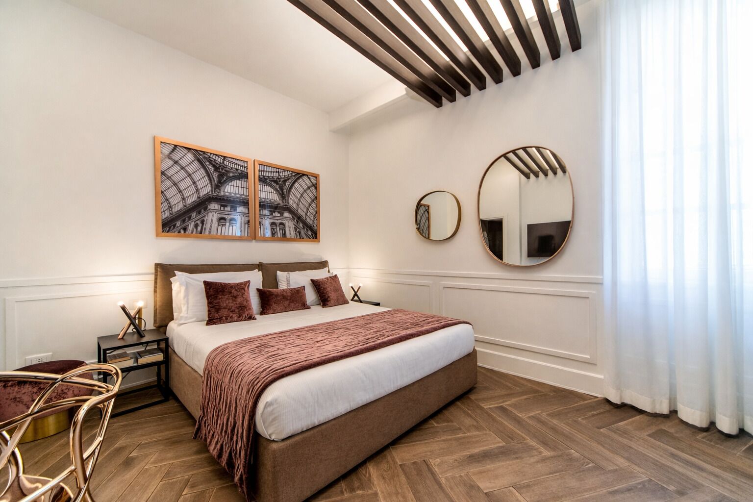 A modern bedroom with a large bed, two framed pictures, a round mirror, and a wooden floor.