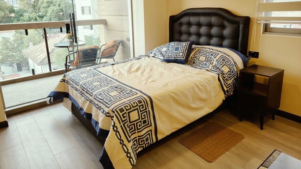 A bedroom with a bed, a nightstand, a chair, and a view of the outside. - Modern studio apartment in downtown area of the city (Cochabamba)
