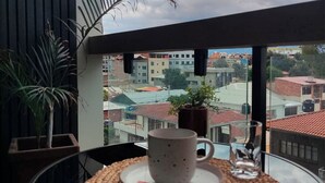 A room with a view of buildings through a window, a table with a mug and a glass, and a potted plant. - Modern studio apartment in downtown area of the city (Cochabamba)