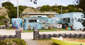 Een klein, lichtblauw gebouw met een bord waarop 'Melshell Oysters' staat. Er is een tafel met stoelen buiten, een klein bootje ervoor en een muurschildering aan de linkerkant.